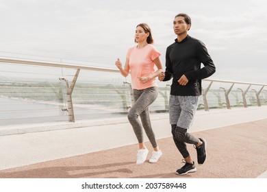 Full length portrait of fit young romantic couple athletes man and woman jogging running together in fitness clothes on city bridge in the morning. Burning calories slimming exercises