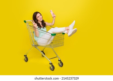 Full length portrait of funny cheerful lady sit trolley make selfie show v-sign isolated on yellow color background