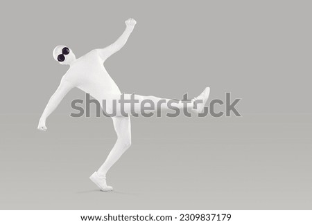 Full length portrait of a funny, happy man in a white, faceless, skintight, spandex bodysuit costume disguise and black, round sunglasses walking or dancing isolated on a grey color background