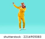 Full length portrait of funny playful showman in yellow suit and rubber pink horse mask dancing on turquoise background. Banner for advertisement, marketing with funky man. He is rising his hands up.