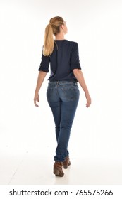 Full length portrait of a girl wearing simple blue shirt and jeans, standing pose facing away on a white background.
