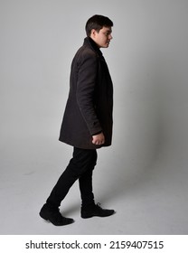  
				Full length portrait of  handsome brunette male model wearing black leather coat. Standing Pose in backwards silhouette  isolated on studio background.