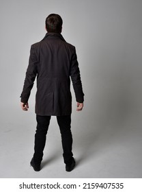  
Full Length Portrait Of  Handsome Brunette Male Model Wearing Black Leather Coat. Standing Pose In Backwards Silhouette  Isolated On Studio Background.