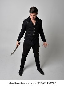 Full length portrait of  handsome brunette male model wearing black shirt and  elegant vest. Standing Pose  holding a sword weapon with gestural hands reaching out,  isolated on studio background.