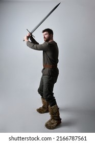Full length portrait of handsome brunette man wearing  historical medieval  viking celtic costume, dynamic  pose holding sword weapon isolated on studio background.
