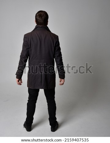  
Full length portrait of  handsome brunette male model wearing black leather coat. Standing Pose in backwards silhouette  isolated on studio background.