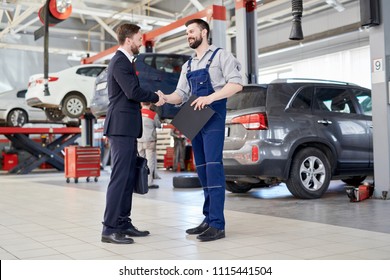 Full Length Portrait Of Handsome Businessman Shaking Hands With Worksman While Standing In Production Workshop Of Modern Car Factory, Copy Space