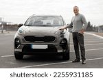 Full length portrait of a handsome imposing 60-70 years old senior man smiling at camera, standing near his newly bought luxury car, in the outdoors parking lot. Looking for new comfortable automobile