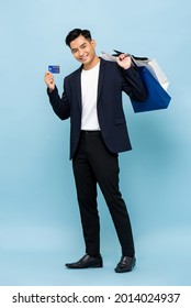 Full Length Portrait Of Handsome Southeast Asian Millenial Man Holding Shopping Bags And Credit Card In Isolated Studio Light Blue Background For Cashless Payment Concept