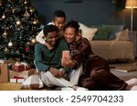 Full length portrait of happy African American family with little boy taking selfie photo via smartphone enjoying cozy Christmas celebration together