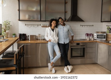 Full length portrait happy African American couple standing in modern kitchen at home, smiling wife and husband excited by relocation, satisfied clients purchased new apartment, mortgage concept