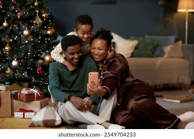 Full length portrait of happy African American family with little boy taking selfie photo via smartphone enjoying cozy Christmas celebration together - Powered by Shutterstock