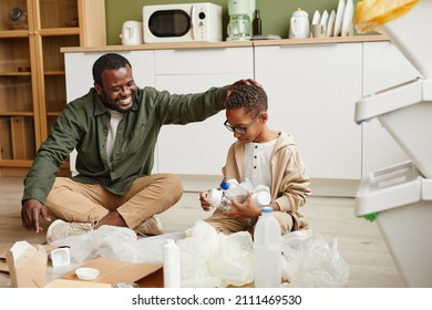 Full length portrait of happy African-American father and son sorting plastic and paper at home for waste recycling, copy space - Powered by Shutterstock