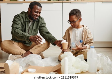 Full length portrait of happy African-American father and son sorting plastic at home for waste recycling, copy space - Powered by Shutterstock