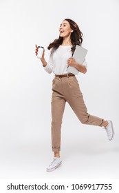 Full length portrait of a happy asian businesswoman carrying laptop computer and cup of coffee to go while running isolated over white background