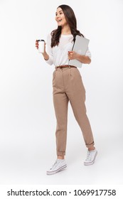 Full Length Portrait Of A Happy Asian Businesswoman Carrying Laptop Computer And Cup Of Coffee To Go While Walking Isolated Over White Background