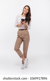 Full length portrait of a happy asian businesswoman using mobile phone isolated over white background
