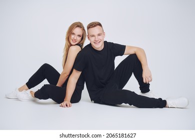 Full length portrait of happy beautiful girl and young man posing cheerfully together in black sportswear on a white background. Fashionable sportswear.