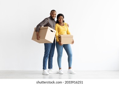 Full Length Portrait Of Happy Black Couple Standing With Cardboard Boxes In Hands In Their New Apartment, Joyful African American Spouses Carrying Belongings After Moving To Own Flat, Copy Space