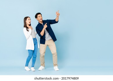 Full length portrait of happy excited Asian couple tourists pointing hands to empty space on isolated light blue background - Shutterstock ID 2017974809