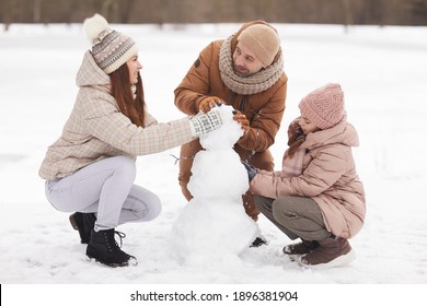 Full length portrait of happy family building snowman together while enjoying walk outdoors in winter, copy space