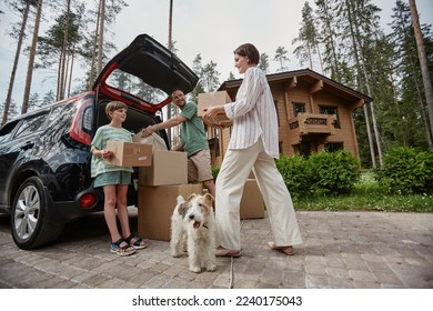 Full length portrait of happy family unloading boxes from car trunk while moving into new house with pet dog - Shutterstock ID 2240175043