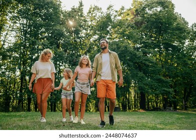 Full length portrait of a happy family of four holding hands while strolling on meadow near forest in nature on sunny summer day. Portrait of a cheerful family taking a walk on a meadow on weekend. - Powered by Shutterstock