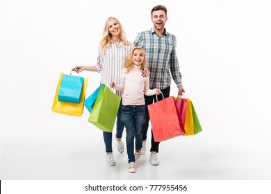 Full Length Portrait Of A Happy Family Holding Paper Shopping Bags While Walking Isolated Over White Background