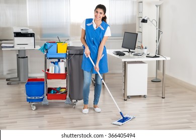 Full Length Portrait Of Happy Female Janitor Mopping Floor In Office