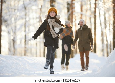 Full Length Portrait Of Happy Little Girl Running Towards Camera In Winter Forest While Enjoying Walk With Family, Copy Space