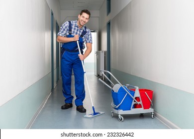 Full Length Portrait Of Happy Male Worker With Broom Cleaning Office Corridor