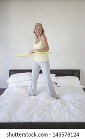 Full Length Portrait Of Happy Middle Aged Woman Holding Hula Hoop On Bed