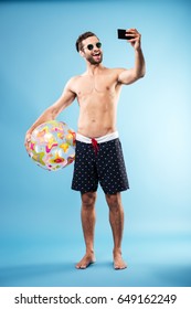 Full Length Portrait Of A Happy Shirtless Guy Holding Beach Ball And Making Selfie Isolated Over Blue