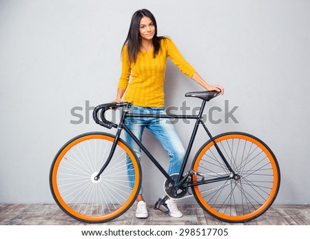 Full length portrait of a happy woman standing near bicycle on gray background. Looking at camera
