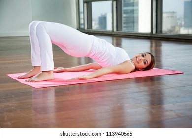 Full length portrait of a happy young woman in Bridge pose on yoga mat