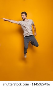 Full length portrait of a happy young man jumping and pointing away isolated over yellow background - Shutterstock ID 1145329436