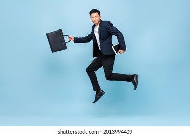 Full length portrait of happy young handsome Asian male office worker running in mid-air holding bag and books in light blue isolated studio background - Shutterstock ID 2013994409