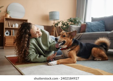 Full length portrait of happy young woman playing with big dog lying on floor in cozy home, copy space - Powered by Shutterstock