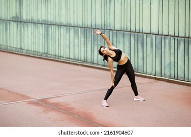 Full Length Portrait Of Healthy Young Woman Doing Sideways Body Stretching Exercise Outside