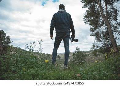 Full length portrait of a hiker man, a traveler photographer holding professional digital camera, admiring the mountains while trekking in the early spring nature - Powered by Shutterstock