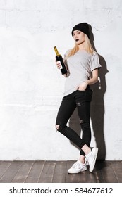 Full length portrait of Hipster girl with bottle of wine which looking at camera with arm at pocket