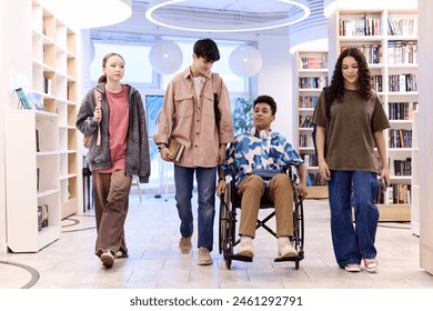 Full length portrait of inclusive group of teenagers walking towards camera in school library - Powered by Shutterstock