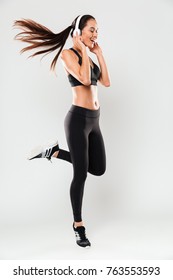 Full Length Portrait Of A Joyful Asian Fitness Woman Wearing Headphones Jumping Isolated Over White Background