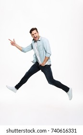 Full length portrait of a joyful happy man jumping and pointing finger away isolated over white background