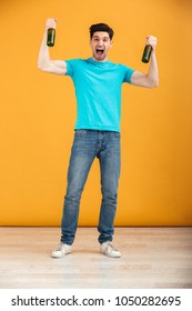 Full Length Portrait Of A Joyful Young Man Holding Two Beer Bottles And Isolated Over Yellow Background