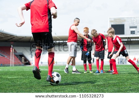 Full length portrait of junior football team practice, back view unrecognizable boy leading ball, copy space