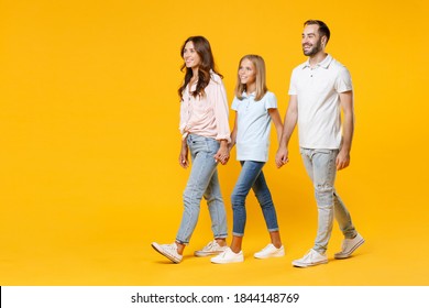 Full Length Portrait Of Laughing Funny Young Parents Mom Dad With Child Kid Daughter Teen Girl In T-shirts Walking Going Holding Hands Looking Aside Isolated On Yellow Background. Family Day Concept