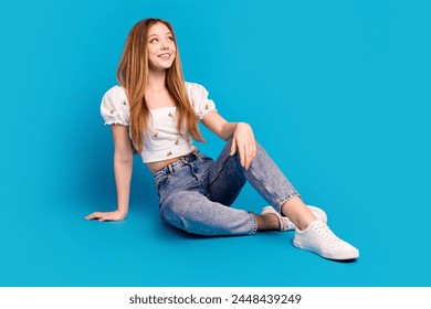 Full length portrait of lovely girl sit floor look think empty space wear top isolated on blue color background - Powered by Shutterstock