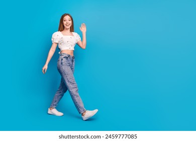 Full length portrait of lovely girl walk hand waving wear top isolated on blue color background - Powered by Shutterstock