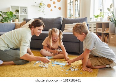 Full length portrait of loving family with special needs child playing board games and puzzles while sitting on floor at home, copy space